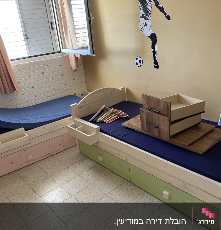 מגירות עץ מונחות על מיטה כחולה בחדר ילדים